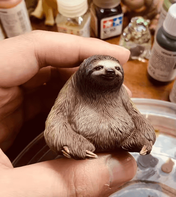 Miniature sloth figure sitting with relaxed arms and calm face, created using white silicone mold